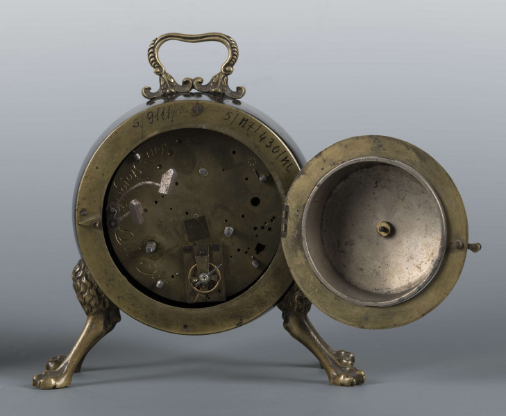 S/Mt/430/ML - Obudowa z brązu w formie bębna leżącego na czterech zwierzęcych łapach, pokrytego czarnym lakierem, z pionowym uchwytem w formie rozciągniętej profilowanej, wolutki. Tarcza zegarowa z mosiądzu, okrągła, moletowana mz malowanymi czarnymi cyframi rzymskimi godzin i oznaczeniem minut; dwie proste wskazówki; osłonieta zamykaną szybką o wypukłym profilu. Zamknięcie z tyłu w postaci okrągłych drzwiczek na zawiasie, z wmontowanym jednym dzwonkiem. Mechanizm mosiężny, o naciągu sprężynowym, z biciem godzin i kwadransów.
Na płycie wewnętrznej mechanizmu grawerowana sygnatura kursywą:
- Jacobus Staigier Lublin
