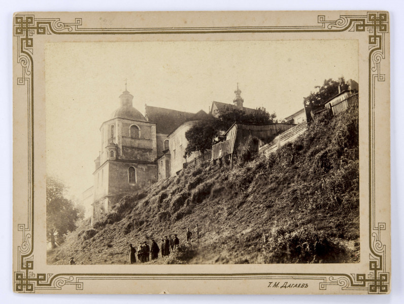 Klasztor dominikanów od strony ulicy Podwale. Po lewej stronie fotografii widoczna bryła świątyni na stromej skarpie. Ujęcie od strony ulicy Podwale na północno-wschodni narożnik Kaplicy Firlejów oraz dachy prezbiterium i nawy głównej z sygnaturką. Po prawej drewniane budynki gospodarcze ogrodzone płotami i osłonięte drzewami. Na dole porośniętej bujną zielenią skarpy grupa ludzi (dorośli i dzieci). 

Fotografia sepiowana, naklejona na tekturę, otoczona ozdobną ramką w kolorze złotym o geometryczno-roślinnych motywach. W p. d. rogu nazwisko autora fotografii w języku rosyjskim. Na rewersie odręczny napis ołówkiem. 
