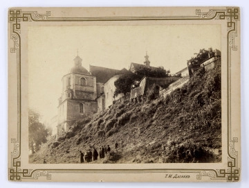 Klasztor dominikanów od strony ulicy Podwale. Po lewej stronie fotografii widoczna bryła świątyni na stromej skarpie. Ujęcie od strony ulicy Podwale na północno-wschodni narożnik Kaplicy Firlejów oraz dachy prezbiterium i nawy głównej z sygnaturką. Po prawej drewniane budynki gospodarcze ogrodzone płotami i osłonięte drzewami. Na dole porośniętej bujną zielenią skarpy grupa ludzi (dorośli i dzieci). 

Fotografia sepiowana, naklejona na tekturę, otoczona ozdobną ramką w kolorze złotym o geometryczno-roślinnych motywach. W p. d. rogu nazwisko autora fotografii w języku rosyjskim. Na rewersie odręczny napis ołówkiem. 
