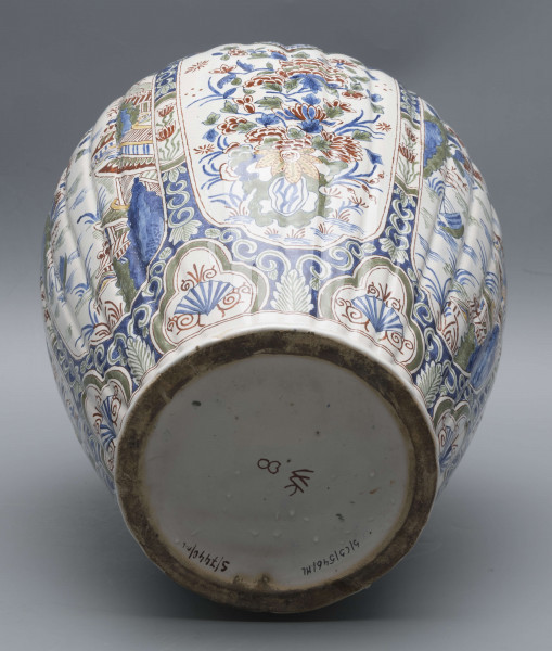 S/CS/546/ML - Wazon owoidalny o niskiej podstawie i niskiej pierścieniowej szyi, powierzchnia drobno kanelowana, pokrywa kopulasta z szerokim kołnierzem, uchwyt w kształcie lwa Fo wspartego prawą łapą na pniu drzewa (?). Dekoracja malowana podszkliwnie w kolorach błękitu, czerwieni, zieleni, żółcieni. W sześciu owalnych, wydłużonych rezerwach na przemian kompozycja kwiatowa z peonią i pejzaż nadrzeczny z architekturą o charakterze orientalnym. U góry - na barkach - sześć owalnych rezerw z kwitnącą gałązką, na dole sześć rezerw trójlistnych z motywem uproszczonej muszli i wolut, na stopie fryz wolutowy, na szyi wąska ukośna kratka. Na pokrywie powtórzona dekoracja z barków, kołnierz biały z fryzem wolutowym analogicznie jak na stopie.
 