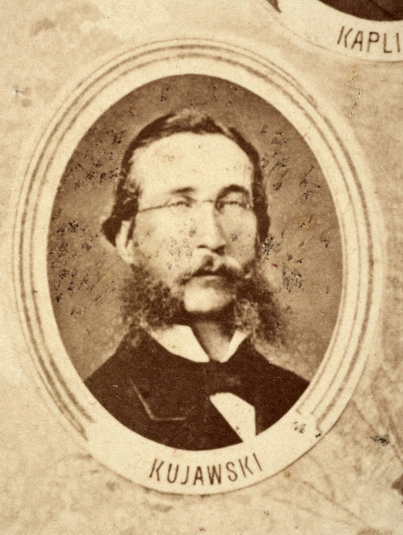 Fotografie w odcieniu sepii umieszczone na tle drzew i roślin, w centralnym miejscu postać kobiety ze sztandarem i aniołkami, wkomponowane widoki budowanej stacji, mostu kolejowego i lokomotywy. Największe zdjęcie w górnej, środkowej części bez podpisu, prawdopodobnie inż. głównej kolei nadwiślańskiej Tadeusz Chrzanowski lub jego następca Walery Titkow. Wśród podobizn pracownicy Biura Głównego Inżyniera: inż. Włodzimierz Stanisławski - pomocnik głównego inżyniera; inż. Feliks Kucharzewski -  pomocnik naczelnika biura; Feliks Kamocki - naczelnik kancelarii; Witold Lanci - naczelnik Wydz. Architektury; dr Wacław Lasocki- służba zdrowia; Władysław Radwan - sprawy zakupu gruntów; inż. Stanisław hr Scipio - projektant mostów kolejowych i jego współpracownicy: inż. Stefan Zieliński, inż. Maurycy Machalski, inż. Feliks Kucharzewski. Fotografia w passe - partout, za szkłem, oprawiona w drewnianą, profilowaną ramę.