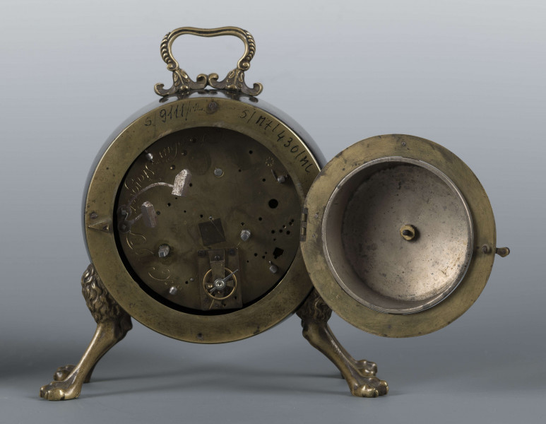 S/Mt/430/ML - Obudowa z brązu w formie bębna leżącego na czterech zwierzęcych łapach, pokrytego czarnym lakierem, z pionowym uchwytem w formie rozciągniętej profilowanej, wolutki. Tarcza zegarowa z mosiądzu, okrągła, moletowana mz malowanymi czarnymi cyframi rzymskimi godzin i oznaczeniem minut; dwie proste wskazówki; osłonieta zamykaną szybką o wypukłym profilu. Zamknięcie z tyłu w postaci okrągłych drzwiczek na zawiasie, z wmontowanym jednym dzwonkiem. Mechanizm mosiężny, o naciągu sprężynowym, z biciem godzin i kwadransów.
Na płycie wewnętrznej mechanizmu grawerowana sygnatura kursywą:
- Jacobus Staigier Lublin
