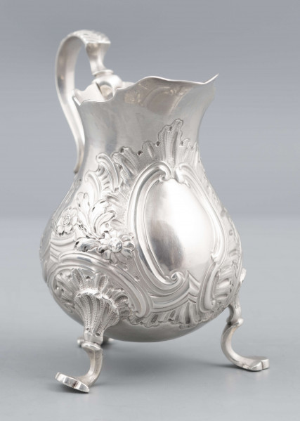 S/Mt/581/ML - Korpus o kształcie gruszkowatym, z wydłużonym wylewem, na trzech nóżkach, ucho profilowane. Krawędź wylewu wycięta faliście, korpus repusowany: na froncie rocaillowy kartusz, po bokach ornamenty wolutowe i kwiatowe.
Na spodzie znaki:
- urząd probierczy w Londynie
- próba Sterling
- oznaczenie roku 