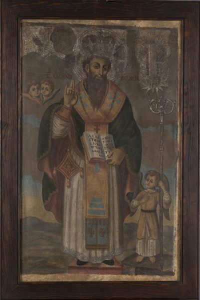 S/Mal/555/ML - Św. Bazyli Wielki w ujęciu całopostaciowym. Święty stoi na różowym podnóżku na tle obłoków oraz górzystego krajobrazu o nisko zarysowanym horyzoncie. Ukazany jest frontalnie, z głową przechyloną lekko w prawo. Prawą dłoń unosi w geście błogosławieństwa, w lewej trzyma księgę otwartą na pisanych cyrylicą słowach ze wspomnienia wieczerzy z Liturgii jego autorstwa: „podał swoim uczniom i apostołom mówiąc: bierzcie ...”. Ubrany jest w szaty biskupie obrządku wschodniego: sticharion wykończony koronką i zebrany u mankietów narękawnikami, u pasa przyczepiony ma złoty epigonation zdobiony wizerunkiem serafina; na sticharion nałożony ma niebieski epitrachilion ze złotymi krzyżami, felonion – zielony ze złotą lamówką od zewnątrz a fioletowy od podbicia, na nim złoty orarion zdobiony niebieskimi krzyżami oraz złoty łańcuch z krzyżem; na otoczonej nimbem głowie ma mitrę. Nimb, mitra oraz ukazane po bokach symbole Ducha Świętego – gołębica nadlatująca w stronę ucha świętego, promienie łączące ją z jego postacią oraz ognista kolumna po prawej stronie są ryte i pokryte srebrzeniem. Przy kolumnie widnieje częściowo zachowany napis cyrylicą: „...  jest Wielki Bazyli”, ponad ramionami świętego widnieje jego imię. Po prawej stronie na odrębnym kamiennym postumencie stoi anioł-akolita ubrany w białą sukienkę z kołnierzem i żółtą tunikę. Trzyma on srebrny pastorał, który w zwieńczeniu przyjmuje formę monogramu chrystusowego. Po lewej na wysokości ramienia św. Bazylego widoczne dwa cherubiny. Całość wtórnie oprawiona w ciemną, masywną, oszczędnie profilowaną ramę.
