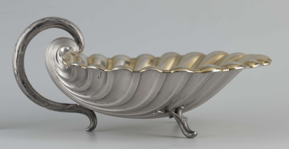 S/Mt/504/ML - Patera z uchwytem, w formie muszli przegrzebka ustawionej poziomo na  dwóch nóżkach - trzecią nóżkę tworzy zakończenie pionowo umocowanego esowatego ucha. 
Na odwrocie sygnatura segmentowa:
- znak miejski Petersburga
- znak imienny złotnika  