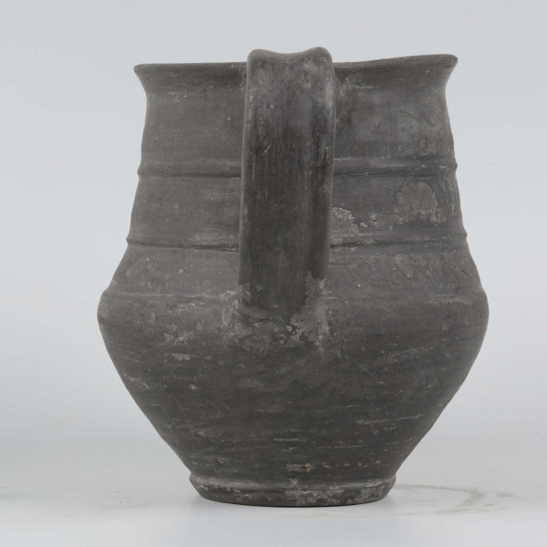 Dno płaskie, wyraźnie wyodrębnione stopką skośnie ściętą ku dołowi; dno wyodrębnione od części przydennej dookolnym wgłębieniem; lekko rozszerzające się ku górze, brzusiec łagodnie zaokraglony, ku górze zwężający się, przechodzący w wysoką, cylindryczną szyjkę; wylew płasko ścięty, rozchylony na zewnątrz; na największej wydętości brzuśca dookolny żłobek; w miejscu przejścia brzuśca w szyję i w połowie szyi dookolny wypukłe listwy; ucho z taśmy środkiem wklęsłej, biegnące od wylewu do załomu brzuśca, szyja zdobiona różnym ornamentem (trzy pasy) przez wygładzenie; powierzchnia gładzona, wyświecona
wymiary dodatkowe: 17,0 cm (obwód); 8,0 cm (śr. dna); 0,3 cm (wys. stopki); 0,5 cm (wys. szyi)