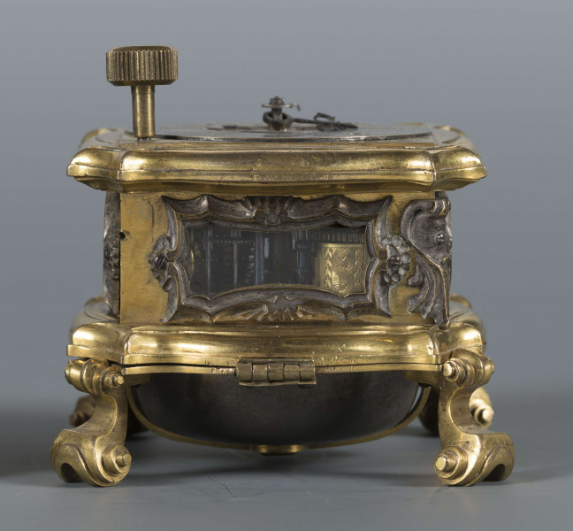 S/Mt/428/ML - Mechanizm o szkielecie płytowym, kwadratowym, łączonym balaskami. Wychwyt szpindlowy regulowany balansem włosowym; napęd sprężynowy chodu ze slimakiem wyrównawczym z funkcją bicia godzin i minut. Umieszczony w szkatule kwadratowej o falistych brzegach, na 4 nóżkach wolutowych; ścianki boczne oszklone w ozdobnie profilowanych ramkach, w narożach ornamenty muszlowo-wolutowe. W tarczy otwory naciągów przysłaniane, w narożniku wyłącznik biciawyłącznik bicia. Pierścień godzinowy srebrzony z rzymskimi oznaczeniemi godzin, arabskimi minut oraz kreskowa skala minutowa. Dwie proste wskazówki: godzinowa i minutowa. Na płycie dolnej mechanizmu obok koka, kółko regulacji chodu zegara: Avance Retard. Dwa młotki w formie muszli, dwie czasze zdwonków koncentrycznie umieszczone w klapie podstawy. 
Pośrodku tarczy dwie plakietki z dzieloną sygnaturą: 