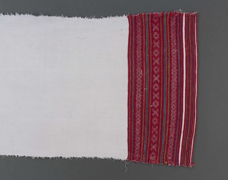 Ręcznik z samodziałowego płótna tkanego splotem prostym. Brzegi dolne, na szer. 14,5 cm, ozdobione ornamentem tkackim zw. pereborami. Ułożony pasowo, złożone z motywów geometrycznych w postaci rombów, kształtów litery X oraz drobnych prążków, w kolorze niebieskim, pomarańczowym i czerwonym.