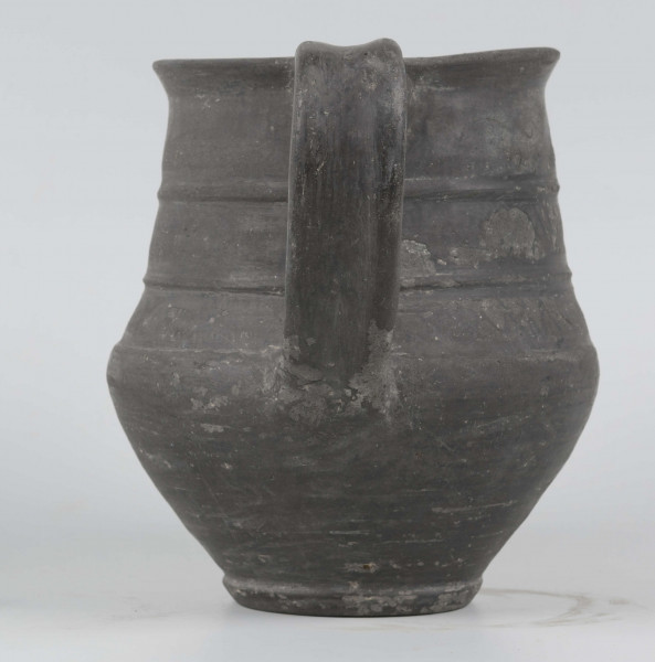 Dno płaskie, wyraźnie wyodrębnione stopką skośnie ściętą ku dołowi; dno wyodrębnione od części przydennej dookolnym wgłębieniem; lekko rozszerzające się ku górze, brzusiec łagodnie zaokraglony, ku górze zwężający się, przechodzący w wysoką, cylindryczną szyjkę; wylew płasko ścięty, rozchylony na zewnątrz; na największej wydętości brzuśca dookolny żłobek; w miejscu przejścia brzuśca w szyję i w połowie szyi dookolny wypukłe listwy; ucho z taśmy środkiem wklęsłej, biegnące od wylewu do załomu brzuśca, szyja zdobiona różnym ornamentem (trzy pasy) przez wygładzenie; powierzchnia gładzona, wyświecona
wymiary dodatkowe: 17,0 cm (obwód); 8,0 cm (śr. dna); 0,3 cm (wys. stopki); 0,5 cm (wys. szyi)