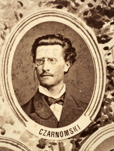 Fotografie w odcieniu sepii umieszczone na tle drzew i roślin, w centralnym miejscu postać kobiety ze sztandarem i aniołkami, wkomponowane widoki budowanej stacji, mostu kolejowego i lokomotywy. Największe zdjęcie w górnej, środkowej części bez podpisu, prawdopodobnie inż. głównej kolei nadwiślańskiej Tadeusz Chrzanowski lub jego następca Walery Titkow. Wśród podobizn pracownicy Biura Głównego Inżyniera: inż. Włodzimierz Stanisławski - pomocnik głównego inżyniera; inż. Feliks Kucharzewski -  pomocnik naczelnika biura; Feliks Kamocki - naczelnik kancelarii; Witold Lanci - naczelnik Wydz. Architektury; dr Wacław Lasocki- służba zdrowia; Władysław Radwan - sprawy zakupu gruntów; inż. Stanisław hr Scipio - projektant mostów kolejowych i jego współpracownicy: inż. Stefan Zieliński, inż. Maurycy Machalski, inż. Feliks Kucharzewski. Fotografia w passe - partout, za szkłem, oprawiona w drewnianą, profilowaną ramę.