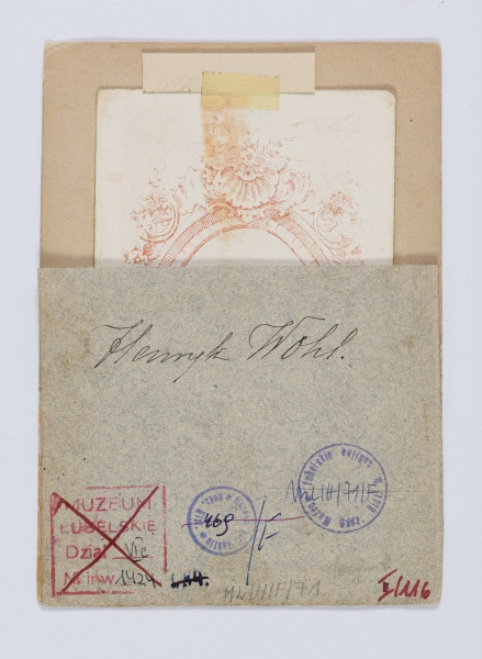 ML/H/F/71 - Fotografia przedstawia dojrzałego mężczyznę zwróconego w prawo. Włosy ciemne, gęste, zaczesane do góry. Wąsy ciemne, dość gęste, łączące się z brodą. Marynarka ciemna z aksamitnym kołnierzem, pod spodem kamizelka i biała koszula. Zdjęcie na firmowym kartoniku zakładu fotograficznego, włożone w passepartout z owalnym wycięciem na fotografię. Na przyklejonym kawałku tekturki w odcieniu szarobłękitnym wypisane czarnym atramentem Henryk Wohl. 