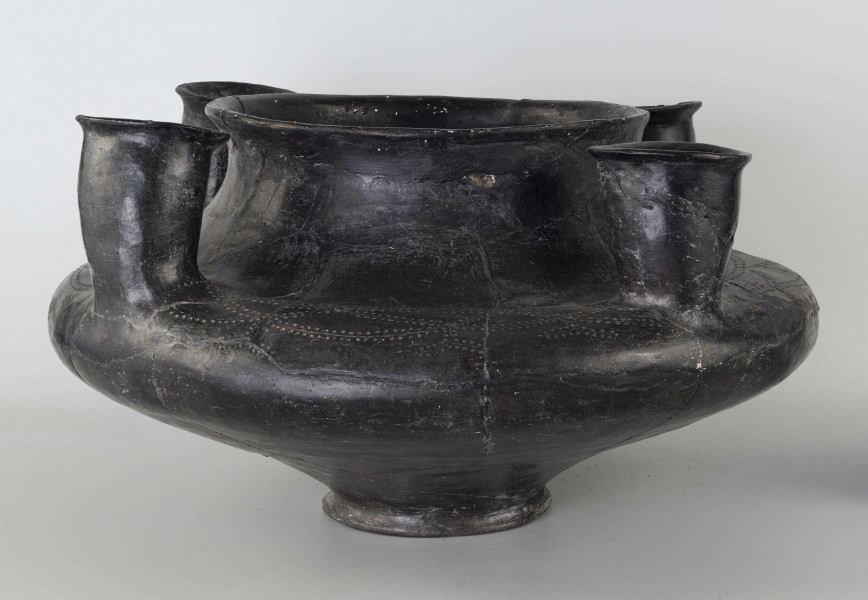 598/A/ML - naczynie kultowe (kernos) kultury pomorskiej; 
wymiary dodatkowe: 25,0 cm - średnica centralnego wylewu
opis: naczynie wazowate o czarnej, błyszczącej powierzchni, którego brzusiec został ozdobiony ornamentem złożonym z linii rytych oraz nakłuć; wokół głównego otworu posiada cztery symetrycznie rozmieszczone kielichy-rytony, które mają nieco wydęte ścianki boczne i kielichowato rozchylone na zewnątrz krawędzie otworów; rytony łączą się z głównym otworem kanalikami; 