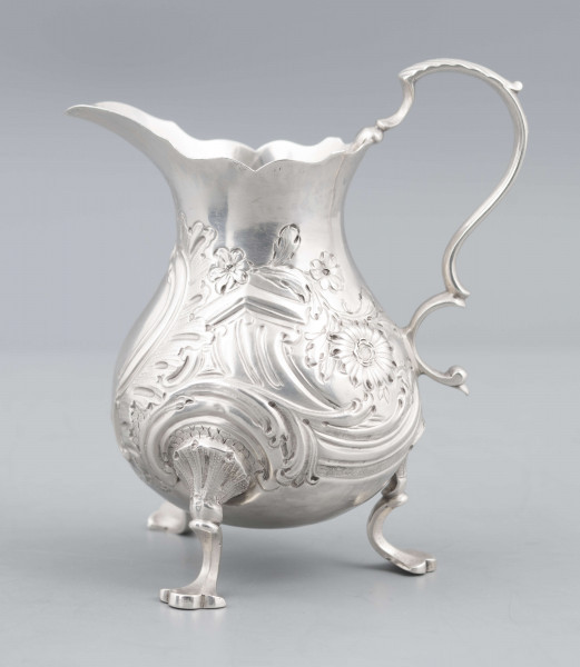 S/Mt/581/ML - Korpus o kształcie gruszkowatym, z wydłużonym wylewem, na trzech nóżkach, ucho profilowane. Krawędź wylewu wycięta faliście, korpus repusowany: na froncie rocaillowy kartusz, po bokach ornamenty wolutowe i kwiatowe.
Na spodzie znaki:
- urząd probierczy w Londynie
- próba Sterling
- oznaczenie roku 