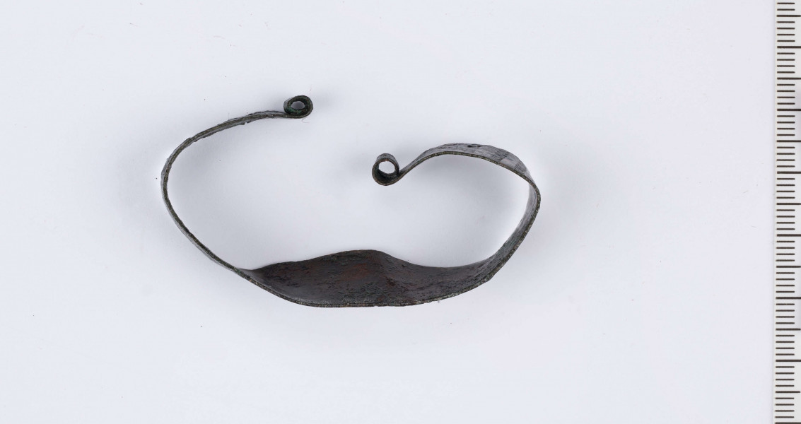 Bransoleta brązowa wykonana z płaskiej taśmy zwężającej się ku końcom.
