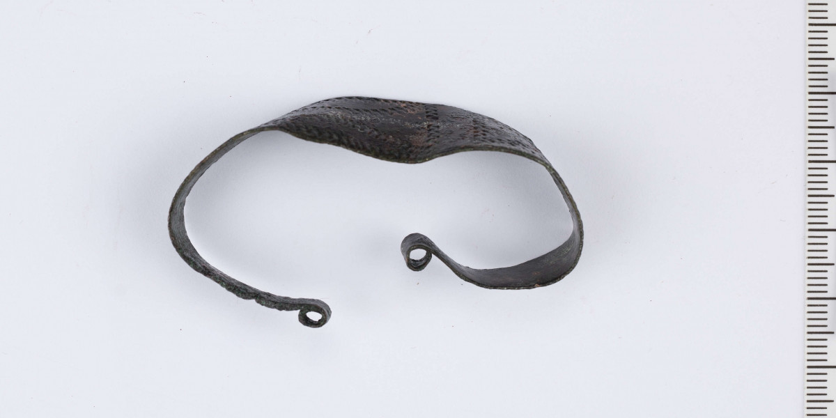 Bransoleta brązowa wykonana z płaskiej taśmy zwężającej się ku końcom.
