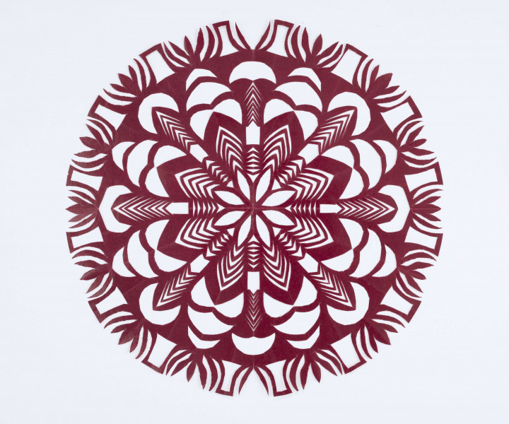 Wycinanka kolista z glansowanego wiśniowego papieru. Ornament geometryczno-roślinny. Środek wycinanki wypełnia ośmiopłatkowy stylizowany kwiat o śred. 13,5 cm o ażurowych płatkach. Motyw otoczony ażurowym ornamentem złożonym z falistych linii i stylizowanych płatków. Zewnętrzny okrąg wycinanki składa się ze stylizowanych wielopłatkowych kwiatków i ażurowych elementów prostokątnych.  