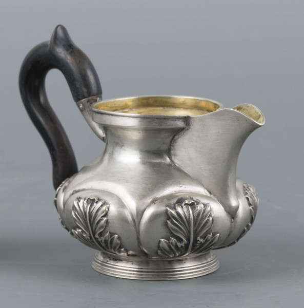 S/Mt/507/ML - Mlecznik w formie spłaszczonej kuli, z krótką szyją, na niskiej pierścieniowatej stopie, wylew prosty z dziobkiem, ucho drewniane esowate ze srebrnymi osadzeniami, pomalowane na czarno. W dolnej części brzuśca sześć pukli wypełnionych repusowanymi lisćmi akantu, wnętrze złocone.
Na spodzie bite punce ze znakami:
- sygnatura 