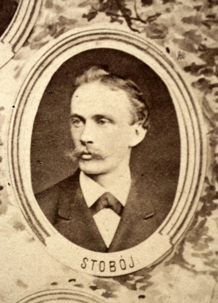 Fotografie w odcieniu sepii umieszczone na tle drzew i roślin, w centralnym miejscu postać kobiety ze sztandarem i aniołkami, wkomponowane widoki budowanej stacji, mostu kolejowego i lokomotywy. Największe zdjęcie w górnej, środkowej części bez podpisu, prawdopodobnie inż. głównej kolei nadwiślańskiej Tadeusz Chrzanowski lub jego następca Walery Titkow. Wśród podobizn pracownicy Biura Głównego Inżyniera: inż. Włodzimierz Stanisławski - pomocnik głównego inżyniera; inż. Feliks Kucharzewski -  pomocnik naczelnika biura; Feliks Kamocki - naczelnik kancelarii; Witold Lanci - naczelnik Wydz. Architektury; dr Wacław Lasocki- służba zdrowia; Władysław Radwan - sprawy zakupu gruntów; inż. Stanisław hr Scipio - projektant mostów kolejowych i jego współpracownicy: inż. Stefan Zieliński, inż. Maurycy Machalski, inż. Feliks Kucharzewski. Fotografia w passe - partout, za szkłem, oprawiona w drewnianą, profilowaną ramę.