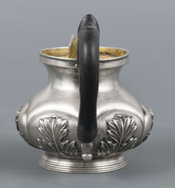 S/Mt/507/ML - Mlecznik w formie spłaszczonej kuli, z krótką szyją, na niskiej pierścieniowatej stopie, wylew prosty z dziobkiem, ucho drewniane esowate ze srebrnymi osadzeniami, pomalowane na czarno. W dolnej części brzuśca sześć pukli wypełnionych repusowanymi lisćmi akantu, wnętrze złocone.
Na spodzie bite punce ze znakami:
- sygnatura 