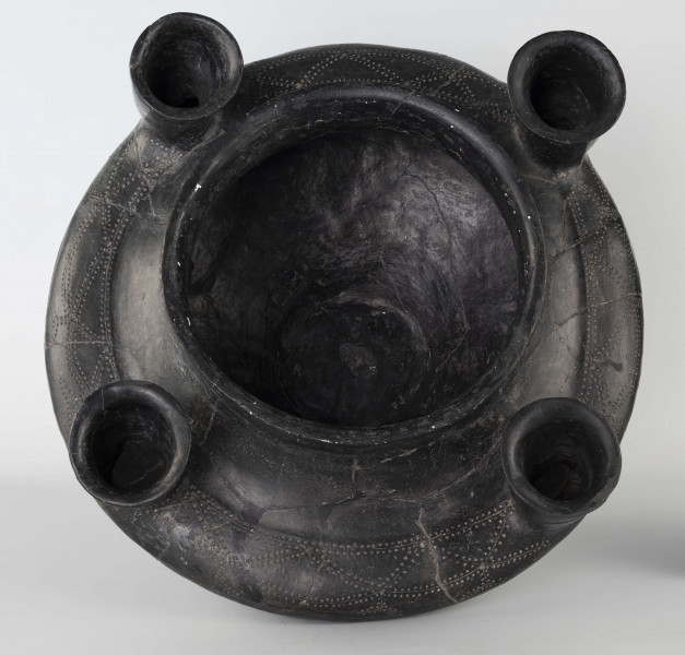 598/A/ML - naczynie kultowe (kernos) kultury pomorskiej; 
wymiary dodatkowe: 25,0 cm - średnica centralnego wylewu
opis: naczynie wazowate o czarnej, błyszczącej powierzchni, którego brzusiec został ozdobiony ornamentem złożonym z linii rytych oraz nakłuć; wokół głównego otworu posiada cztery symetrycznie rozmieszczone kielichy-rytony, które mają nieco wydęte ścianki boczne i kielichowato rozchylone na zewnątrz krawędzie otworów; rytony łączą się z głównym otworem kanalikami; 