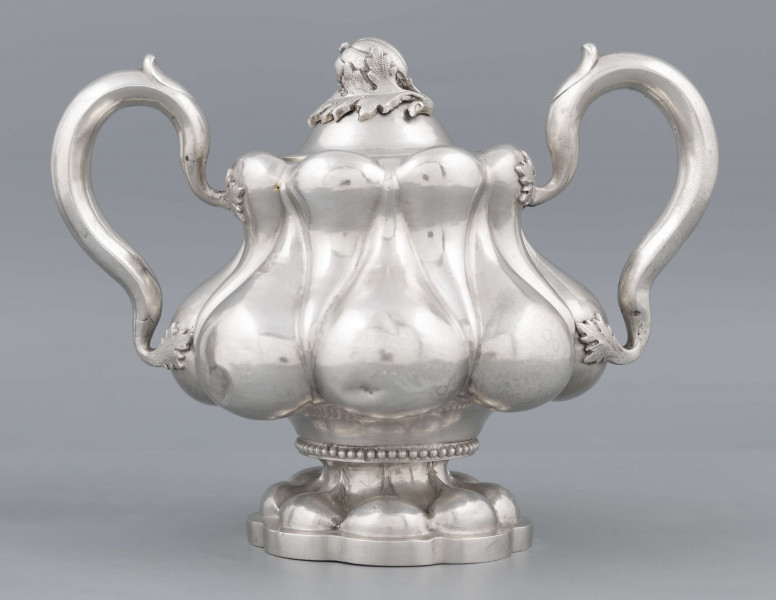 S/Mt/392/ML - Stopa ośmiolistna z ośmioma wydatnymi puklami; trzon krótki zdobiony rzedem perełek; korpus gruszkowaty pokryty dwoma rzędami pukli w formie kropel - większe na dole, mniejsze u góry; po bokach dwa ucha w formie litery 