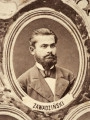 Fotografie w odcieniu sepii umieszczone na tle drzew i roślin, w centralnym miejscu postać kobiety ze sztandarem i aniołkami, wkomponowane widoki budowanej stacji, mostu kolejowego i lokomotywy. Największe zdjęcie w górnej, środkowej części bez podpisu, prawdopodobnie inż. głównej kolei nadwiślańskiej Tadeusz Chrzanowski lub jego następca Walery Titkow. Wśród podobizn pracownicy Biura Głównego Inżyniera: inż. Włodzimierz Stanisławski - pomocnik głównego inżyniera; inż. Feliks Kucharzewski -  pomocnik naczelnika biura; Feliks Kamocki - naczelnik kancelarii; Witold Lanci - naczelnik Wydz. Architektury; dr Wacław Lasocki- służba zdrowia; Władysław Radwan - sprawy zakupu gruntów; inż. Stanisław hr Scipio - projektant mostów kolejowych i jego współpracownicy: inż. Stefan Zieliński, inż. Maurycy Machalski, inż. Feliks Kucharzewski. Fotografia w passe - partout, za szkłem, oprawiona w drewnianą, profilowaną ramę.