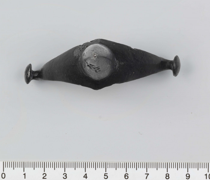 1044/A/ML/1 - Ostroga żelazna z wklęsłym do wewnątrz, łukowatym kabłąkiem. Szeroki przy nasadzie kolca kabłąk zwęża sie stopniowo, przechodząc w wałkowate wygięcia zaczepu, zakończone soczewkowatymi guzkami. Kolec częściowo pusty, ma kształt przegiętego nieznacznie, facetowanego stożka. Przy nasadzie dwie wypiłowane bruzdy z gęsto poprzecznie nacinanym grzbietem powstałym między nimi. Ostroga stanowi element wyposażenia ciałopalnego pochówku złożonego prawdopodobnie w popielnicy. Odkrycia dokonano w 1959 roku przypadkowo w czasie prac rolnych. Oprócz trzech grotów, pochówkowi wojownika towarzyszyły: żelazne umbo, dwie ostrogi, tok brązowy (prawdopodobnie okucie drzewca oszczepu) a także żelazny miecz z miedziana inkrustacją wyobrażającą rzymskich bogów. Pochowany na terenie obecnej wsi Podlodów wojownik należał do elity wojskowej przedstawicieli kultury przeworskiej.
Wymiary dodatkowe: 1,6 cm (podstawa kolca); 1,0 cm (śr. guzków); 3,2 cm (szer. kabłąka przy nasadzie kolca); 0,5 cm (szer. kabłaka przy zaczepach)