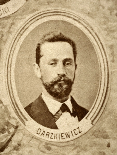 Fotografie w odcieniu sepii umieszczone na tle drzew i roślin, w centralnym miejscu postać kobiety ze sztandarem i aniołkami, wkomponowane widoki budowanej stacji, mostu kolejowego i lokomotywy. Największe zdjęcie w górnej, środkowej części bez podpisu, prawdopodobnie inż. głównej kolei nadwiślańskiej Tadeusz Chrzanowski lub jego następca Walery Titkow. Wśród podobizn pracownicy Biura Głównego Inżyniera: inż. Włodzimierz Stanisławski - pomocnik głównego inżyniera; inż. Feliks Kucharzewski -  pomocnik naczelnika biura; Feliks Kamocki - naczelnik kancelarii; Witold Lanci - naczelnik Wydz. Architektury; dr Wacław Lasocki- służba zdrowia; Władysław Radwan - sprawy zakupu gruntów; inż. Stanisław hr Scipio - projektant mostów kolejowych i jego współpracownicy: inż. Stefan Zieliński, inż. Maurycy Machalski, inż. Feliks Kucharzewski. Fotografia w passe - partout, za szkłem, oprawiona w drewnianą, profilowaną ramę.
