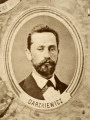 Fotografie w odcieniu sepii umieszczone na tle drzew i roślin, w centralnym miejscu postać kobiety ze sztandarem i aniołkami, wkomponowane widoki budowanej stacji, mostu kolejowego i lokomotywy. Największe zdjęcie w górnej, środkowej części bez podpisu, prawdopodobnie inż. głównej kolei nadwiślańskiej Tadeusz Chrzanowski lub jego następca Walery Titkow. Wśród podobizn pracownicy Biura Głównego Inżyniera: inż. Włodzimierz Stanisławski - pomocnik głównego inżyniera; inż. Feliks Kucharzewski -  pomocnik naczelnika biura; Feliks Kamocki - naczelnik kancelarii; Witold Lanci - naczelnik Wydz. Architektury; dr Wacław Lasocki- służba zdrowia; Władysław Radwan - sprawy zakupu gruntów; inż. Stanisław hr Scipio - projektant mostów kolejowych i jego współpracownicy: inż. Stefan Zieliński, inż. Maurycy Machalski, inż. Feliks Kucharzewski. Fotografia w passe - partout, za szkłem, oprawiona w drewnianą, profilowaną ramę.