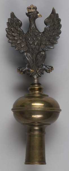 ML/H/200 - Sztandar Przedszkola i Seminarium Ochroniarskiego Marii Papiewskiej. Sztandar w formie kwadratu zszytego z dwóch kawałków ozdobnej tkaniny, obszyty frędzlami. Wzdłuż jednej z krawędzi mocowania w formie troczków do zaczepienia na drzewcu. Na awersie pośrodku tkaniny w kremowym kolorze w kwiatowe motywy herb miasta Lublina (koziołek wsparty o winną latorośl umieszczony na czerwonym polu na tarczy zwieńczonej koroną) oraz haftowany w półkolu czerwoną nicią napis z nazwą posiadacza. Na rewersie pośrodku wzorzystej tkaniny w kolorze czerwonym haftowany biały orzeł w złotej koronie wysadzanej klejnotami z umieszczoną poniżej haftowaną w kolorze złotym datą 1916 r. Metalowa głowica w kształcie orła w koronie umocowanego na kuli. Dodatkowo materiałowy pokrowiec zapinany u góry na napy i haftki, w kolorze zielonkawym, z wyhaftowanym pośrodku napisem w kolorze żółtym.