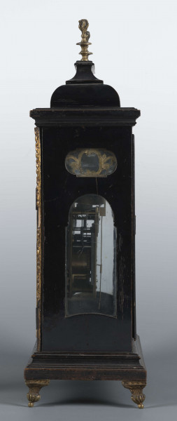 S/Mt/531/ML - Obudowa szafkowa, czworoboczna ze schodkowym zwieńczeniem, pokryta czarną politurą, oszklona z czterech stron, na czterech nóżkach z mosiądzu; w górnych narożnikach mosiężne sterczyny w formie płonących wazonów. Mechanizm chodu i bicia o napędzie sprężynowym, z wahadłem i dwoma dzwonkami; bicie godzin i kwadransów, budzik i repetier. Tarcza biało emaliowana z czarnymi cyframi arabskimi godzin i minut, w niej trzy otwory na osie sprężyn; trzy wskazówki, godzinowa i minutowa - ozdobne, sekundowa prosta. W górnej części tarczy sygnatura pisana ozdobną kursywą: M.G. / Jurkiewicz /  w Lublinie. Powyżej tarczy wycięcie z widocznym wahadełkiem kontrolnym i trzy mniejsze emaliowane tarcze: środkowa z miniaturą pejzażową, boczne z wyłączeniem chodu i bicia.