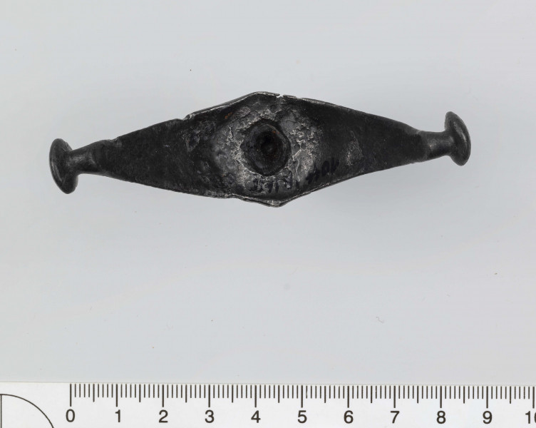 1044/A/ML/1 - Ostroga żelazna z wklęsłym do wewnątrz, łukowatym kabłąkiem. Szeroki przy nasadzie kolca kabłąk zwęża sie stopniowo, przechodząc w wałkowate wygięcia zaczepu, zakończone soczewkowatymi guzkami. Kolec częściowo pusty, ma kształt przegiętego nieznacznie, facetowanego stożka. Przy nasadzie dwie wypiłowane bruzdy z gęsto poprzecznie nacinanym grzbietem powstałym między nimi. Ostroga stanowi element wyposażenia ciałopalnego pochówku złożonego prawdopodobnie w popielnicy. Odkrycia dokonano w 1959 roku przypadkowo w czasie prac rolnych. Oprócz trzech grotów, pochówkowi wojownika towarzyszyły: żelazne umbo, dwie ostrogi, tok brązowy (prawdopodobnie okucie drzewca oszczepu) a także żelazny miecz z miedziana inkrustacją wyobrażającą rzymskich bogów. Pochowany na terenie obecnej wsi Podlodów wojownik należał do elity wojskowej przedstawicieli kultury przeworskiej.
Wymiary dodatkowe: 1,6 cm (podstawa kolca); 1,0 cm (śr. guzków); 3,2 cm (szer. kabłąka przy nasadzie kolca); 0,5 cm (szer. kabłaka przy zaczepach)