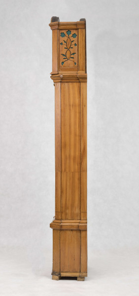 Tarcza w kształcie kwadratu zwieńczonego półkolem, złocona, w narożach ornamenty odlewane z brązu, złocone; pierścień  godzinowy srebrzony z rzymskimi oznaczeniami godzin i zaznaczonymi minutami, wewnątrz tarcza sekundnika, tarczka budzika, plakietka z sygnaturą 