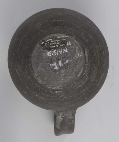 Dno płaskie, wyraźnie wyodrębnione stopką skośnie ściętą ku dołowi; dno wyodrębnione od części przydennej dookolnym wgłębieniem; lekko rozszerzające się ku górze, brzusiec łagodnie zaokraglony, ku górze zwężający się, przechodzący w wysoką, cylindryczną szyjkę; wylew płasko ścięty, rozchylony na zewnątrz; na największej wydętości brzuśca dookolny żłobek; w miejscu przejścia brzuśca w szyję i w połowie szyi dookolny wypukłe listwy; ucho z taśmy środkiem wklęsłej, biegnące od wylewu do załomu brzuśca, szyja zdobiona różnym ornamentem (trzy pasy) przez wygładzenie; powierzchnia gładzona, wyświecona
wymiary dodatkowe: 17,0 cm (obwód); 8,0 cm (śr. dna); 0,3 cm (wys. stopki); 0,5 cm (wys. szyi)