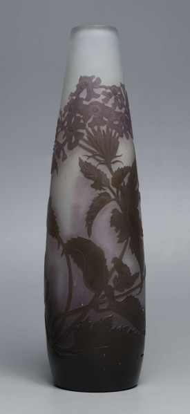 S/CS/1620/ML - Wazon o kształcie wrzecionowatym ze szkła grubościennego, matowego, bezbarwnego,  podbarwionego od dołu fioletem, od góry błękitem. Powlekany warstwą liliową i brązowooliwkową; w niej trawiona i polerowana dekoracja roślinna: swobodnie rozmieszczone gałązki werbeny z kwiatami.
 