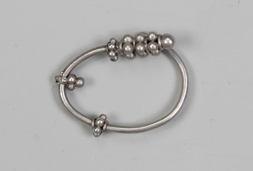 169/A/ML/1 - Zausznica srebrna składa się z kabłąka, na którym zawieszono wisiorek o winogronowatym kształcie. Ozdoby tego typu charakteryzują się kabłąkiem o jednym końcu ucięty prosto, drugim zaś zwiniętym w oczko. W połowie wysokości kabłąka znajdują się wieńce wykonane z granulek ograniczonych pierścieniami z drutu. W dolnej części kabłąka występuje wisiorek uformowany z kilku wieńców granulek zwieńczony granulką osadzoną na pierścieniu z drutu. 