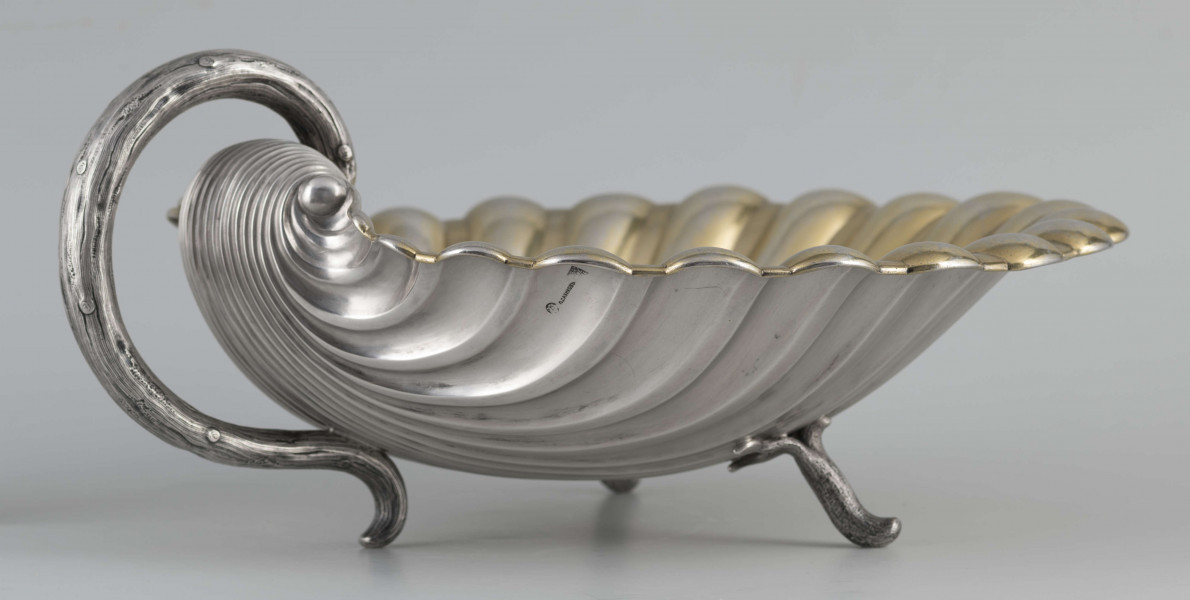 S/Mt/504/ML - Patera z uchwytem, w formie muszli przegrzebka ustawionej poziomo na  dwóch nóżkach - trzecią nóżkę tworzy zakończenie pionowo umocowanego esowatego ucha. 
Na odwrocie sygnatura segmentowa:
- znak miejski Petersburga
- znak imienny złotnika  