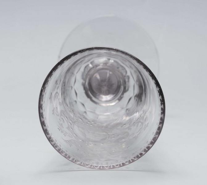 S/CS/244/ML - Stopa okrągła, lekko uniesiona, trzon tralkowy, z pęcherzykiem powietrza, fasetowany, od czaszy oddzielony pierścieniem i dwoma talerzykami, czasza stozkowata, u nasady zaokrąglona, szlifowana w dwa pionowe rzędy owalnych faset. Dekoracja rytowana: na czaszy dwustronna - z jednej strony owalna tarcza z parą gołąbków połączonych dziobkami stojących na serduszkach w rozbudowanym kartuszu z uszakami, z którego wyrastaja gałązki; po drugiej stronie litery 