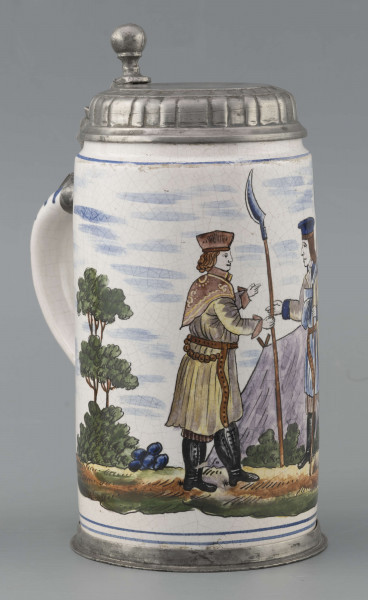 S/CS/64/ML - Korpus cylindryczny z uchem w kształcie litery „C”, pokrywka cynowa, płaska z profilowanym brzegiem i kulistą sterczyną  na zawiasie umocowanym do ucha; profilowana cynowa obręcz otacza dolną krawędź. Pokryty białym szkliwem z wielobarwną dekoracją malowaną skomponowaną przeciwlegle do ucha. Przedstawia ona w uproszczony sposób scenę w obozie  wojskowym: dwaj uzbrojeni kosynierzy stoją na wprost siebie, za nimi widoczny namiot a wokół zielone zarośla i drzewa. Niebo zaznaczone błękitnymi plamami, w tym samym kolorze malowane paski obiegają krawędzie naczynia i zdobią ucho. Tematyka przedstawienia ma wyraźnie patriotyczny charakter nawiązując do powstania kościuszkowskiego.

