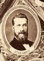 Fotografie w odcieniu sepii umieszczone na tle drzew i roślin, w centralnym miejscu postać kobiety ze sztandarem i aniołkami, wkomponowane widoki budowanej stacji, mostu kolejowego i lokomotywy. Największe zdjęcie w górnej, środkowej części bez podpisu, prawdopodobnie inż. głównej kolei nadwiślańskiej Tadeusz Chrzanowski lub jego następca Walery Titkow. Wśród podobizn pracownicy Biura Głównego Inżyniera: inż. Włodzimierz Stanisławski - pomocnik głównego inżyniera; inż. Feliks Kucharzewski -  pomocnik naczelnika biura; Feliks Kamocki - naczelnik kancelarii; Witold Lanci - naczelnik Wydz. Architektury; dr Wacław Lasocki- służba zdrowia; Władysław Radwan - sprawy zakupu gruntów; inż. Stanisław hr Scipio - projektant mostów kolejowych i jego współpracownicy: inż. Stefan Zieliński, inż. Maurycy Machalski, inż. Feliks Kucharzewski. Fotografia w passe - partout, za szkłem, oprawiona w drewnianą, profilowaną ramę.