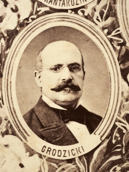 Fotografie w odcieniu sepii umieszczone na tle drzew i roślin, w centralnym miejscu postać kobiety ze sztandarem i aniołkami, wkomponowane widoki budowanej stacji, mostu kolejowego i lokomotywy. Największe zdjęcie w górnej, środkowej części bez podpisu, prawdopodobnie inż. głównej kolei nadwiślańskiej Tadeusz Chrzanowski lub jego następca Walery Titkow. Wśród podobizn pracownicy Biura Głównego Inżyniera: inż. Włodzimierz Stanisławski - pomocnik głównego inżyniera; inż. Feliks Kucharzewski -  pomocnik naczelnika biura; Feliks Kamocki - naczelnik kancelarii; Witold Lanci - naczelnik Wydz. Architektury; dr Wacław Lasocki- służba zdrowia; Władysław Radwan - sprawy zakupu gruntów; inż. Stanisław hr Scipio - projektant mostów kolejowych i jego współpracownicy: inż. Stefan Zieliński, inż. Maurycy Machalski, inż. Feliks Kucharzewski. Fotografia w passe - partout, za szkłem, oprawiona w drewnianą, profilowaną ramę.