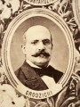 Fotografie w odcieniu sepii umieszczone na tle drzew i roślin, w centralnym miejscu postać kobiety ze sztandarem i aniołkami, wkomponowane widoki budowanej stacji, mostu kolejowego i lokomotywy. Największe zdjęcie w górnej, środkowej części bez podpisu, prawdopodobnie inż. głównej kolei nadwiślańskiej Tadeusz Chrzanowski lub jego następca Walery Titkow. Wśród podobizn pracownicy Biura Głównego Inżyniera: inż. Włodzimierz Stanisławski - pomocnik głównego inżyniera; inż. Feliks Kucharzewski -  pomocnik naczelnika biura; Feliks Kamocki - naczelnik kancelarii; Witold Lanci - naczelnik Wydz. Architektury; dr Wacław Lasocki- służba zdrowia; Władysław Radwan - sprawy zakupu gruntów; inż. Stanisław hr Scipio - projektant mostów kolejowych i jego współpracownicy: inż. Stefan Zieliński, inż. Maurycy Machalski, inż. Feliks Kucharzewski. Fotografia w passe - partout, za szkłem, oprawiona w drewnianą, profilowaną ramę.