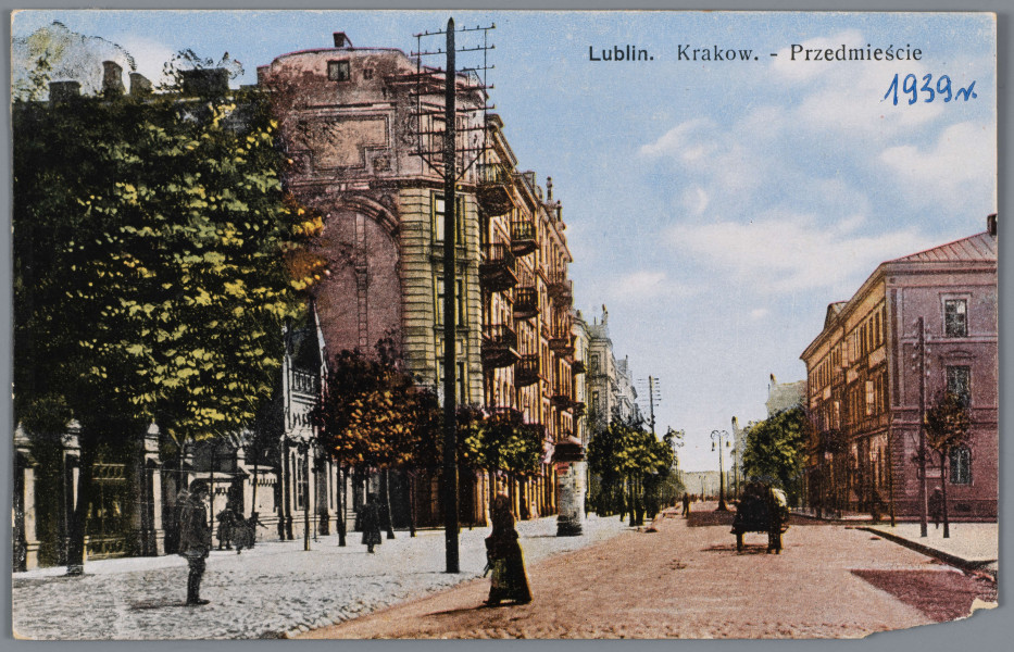 ML/H/3982 - Pocztówka barwna z widokiem ulicy Krakowskie Przedmieście przy skrzyżowaniu z ulicą Lipową i parkanem Ogrodu Saskiego. Na pierwszym planie zabudowania kamienic po obu stronach. Ujęcie w poziomie, z perspektywy. Z lewej strony szeroki chodnik, słup telegraficzny, wejście do Ogrodu Saskiego wraz z ogrodzeniem i domkiem stróża. Widoczne drzewa w parku. Dalej wysokie kamienice, rząd drzew i słup ogłoszeniowy. Po prawej stronie skrzyżowanie z ulicą Lipową, fragment chodnika i kamienice. Na pierwszym planie kobieta przechodząca przez ulicę. Na chodniku stojący mężczyzna. Na środku ulicy bryczka. W p.g. rogu napis informacyjny czarnym drukiem oraz data niebieskim długopisem. Na rewersie ślady po naklejeniu na papier. U dołu logo wydawcy nadrukiem w kolorze brązowym. W p.d. rogu drukiem data wydania i numer serii wydawniczej.