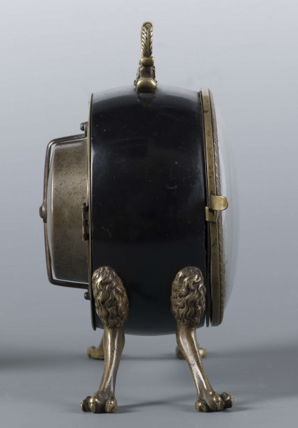 S/Mt/430/ML - Obudowa z brązu w formie bębna leżącego na czterech zwierzęcych łapach, pokrytego czarnym lakierem, z pionowym uchwytem w formie rozciągniętej profilowanej, wolutki. Tarcza zegarowa z mosiądzu, okrągła, moletowana mz malowanymi czarnymi cyframi rzymskimi godzin i oznaczeniem minut; dwie proste wskazówki; osłonieta zamykaną szybką o wypukłym profilu. Zamknięcie z tyłu w postaci okrągłych drzwiczek na zawiasie, z wmontowanym jednym dzwonkiem. Mechanizm mosiężny, o naciągu sprężynowym, z biciem godzin i kwadransów.
Na płycie wewnętrznej mechanizmu grawerowana sygnatura kursywą:
- Jacobus Staigier Lublin
