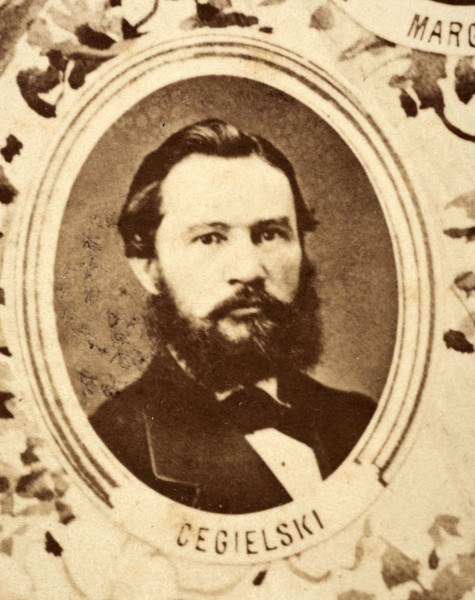 Fotografie w odcieniu sepii umieszczone na tle drzew i roślin, w centralnym miejscu postać kobiety ze sztandarem i aniołkami, wkomponowane widoki budowanej stacji, mostu kolejowego i lokomotywy. Największe zdjęcie w górnej, środkowej części bez podpisu, prawdopodobnie inż. głównej kolei nadwiślańskiej Tadeusz Chrzanowski lub jego następca Walery Titkow. Wśród podobizn pracownicy Biura Głównego Inżyniera: inż. Włodzimierz Stanisławski - pomocnik głównego inżyniera; inż. Feliks Kucharzewski -  pomocnik naczelnika biura; Feliks Kamocki - naczelnik kancelarii; Witold Lanci - naczelnik Wydz. Architektury; dr Wacław Lasocki- służba zdrowia; Władysław Radwan - sprawy zakupu gruntów; inż. Stanisław hr Scipio - projektant mostów kolejowych i jego współpracownicy: inż. Stefan Zieliński, inż. Maurycy Machalski, inż. Feliks Kucharzewski. Fotografia w passe - partout, za szkłem, oprawiona w drewnianą, profilowaną ramę.