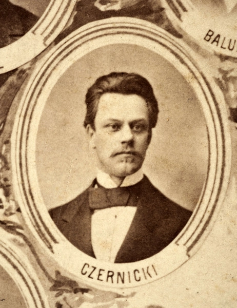 Fotografie w odcieniu sepii umieszczone na tle drzew i roślin, w centralnym miejscu postać kobiety ze sztandarem i aniołkami, wkomponowane widoki budowanej stacji, mostu kolejowego i lokomotywy. Największe zdjęcie w górnej, środkowej części bez podpisu, prawdopodobnie inż. głównej kolei nadwiślańskiej Tadeusz Chrzanowski lub jego następca Walery Titkow. Wśród podobizn pracownicy Biura Głównego Inżyniera: inż. Włodzimierz Stanisławski - pomocnik głównego inżyniera; inż. Feliks Kucharzewski -  pomocnik naczelnika biura; Feliks Kamocki - naczelnik kancelarii; Witold Lanci - naczelnik Wydz. Architektury; dr Wacław Lasocki- służba zdrowia; Władysław Radwan - sprawy zakupu gruntów; inż. Stanisław hr Scipio - projektant mostów kolejowych i jego współpracownicy: inż. Stefan Zieliński, inż. Maurycy Machalski, inż. Feliks Kucharzewski. Fotografia w passe - partout, za szkłem, oprawiona w drewnianą, profilowaną ramę.