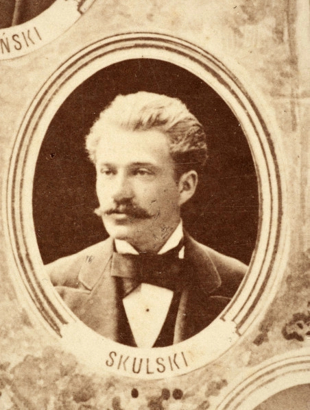 Fotografie w odcieniu sepii umieszczone na tle drzew i roślin, w centralnym miejscu postać kobiety ze sztandarem i aniołkami, wkomponowane widoki budowanej stacji, mostu kolejowego i lokomotywy. Największe zdjęcie w górnej, środkowej części bez podpisu, prawdopodobnie inż. głównej kolei nadwiślańskiej Tadeusz Chrzanowski lub jego następca Walery Titkow. Wśród podobizn pracownicy Biura Głównego Inżyniera: inż. Włodzimierz Stanisławski - pomocnik głównego inżyniera; inż. Feliks Kucharzewski -  pomocnik naczelnika biura; Feliks Kamocki - naczelnik kancelarii; Witold Lanci - naczelnik Wydz. Architektury; dr Wacław Lasocki- służba zdrowia; Władysław Radwan - sprawy zakupu gruntów; inż. Stanisław hr Scipio - projektant mostów kolejowych i jego współpracownicy: inż. Stefan Zieliński, inż. Maurycy Machalski, inż. Feliks Kucharzewski. Fotografia w passe - partout, za szkłem, oprawiona w drewnianą, profilowaną ramę.