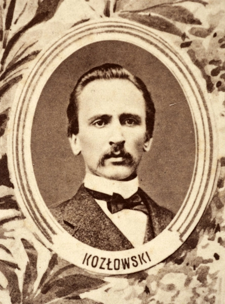 Fotografie w odcieniu sepii umieszczone na tle drzew i roślin, w centralnym miejscu postać kobiety ze sztandarem i aniołkami, wkomponowane widoki budowanej stacji, mostu kolejowego i lokomotywy. Największe zdjęcie w górnej, środkowej części bez podpisu, prawdopodobnie inż. głównej kolei nadwiślańskiej Tadeusz Chrzanowski lub jego następca Walery Titkow. Wśród podobizn pracownicy Biura Głównego Inżyniera: inż. Włodzimierz Stanisławski - pomocnik głównego inżyniera; inż. Feliks Kucharzewski -  pomocnik naczelnika biura; Feliks Kamocki - naczelnik kancelarii; Witold Lanci - naczelnik Wydz. Architektury; dr Wacław Lasocki- służba zdrowia; Władysław Radwan - sprawy zakupu gruntów; inż. Stanisław hr Scipio - projektant mostów kolejowych i jego współpracownicy: inż. Stefan Zieliński, inż. Maurycy Machalski, inż. Feliks Kucharzewski. Fotografia w passe - partout, za szkłem, oprawiona w drewnianą, profilowaną ramę.