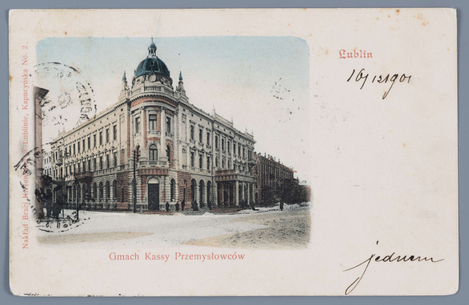 ML/H/1218 - Pocztówka barwna z widokiem na gmach dawnej lubelskiej Kasy Przemysłowców (w okresie międzywojennym „Lublinianka”, dziś „Grand Hotel”). Widok od strony placu Litewskiego na narożnik budynku zwieńczony kopułą i wieżyczkami. Ściany w kolorach ceglastym i białym. Elementy dachu ciemnoniebieskie. Na ulicy miejscami odgarnięty śnieg. Na chodniku ciemne sylwetki przechodniów. Z lewej strony fragment kamienicy. Po prawej pierzeja Krakowskiego Przedmieścia. Podkolorowane zdjęcie, o zaokrąglonych krawędziach, umieszczone na białym tle po lewej stronie. Napisy informacyjne czerwonym drukiem rozmieszczone wokół ilustracji – pod zdjęciem tytuł, wzdłuż lewej krawędzi nazwa nakładcy, w p.g. rogu miejsce powstania. Na białym polu po lewej odręczne napisy czarnym atramentem. Mało czytelne trzy stemple pocztowe. Na rewersie czarna linatura z odręczną korespondencją. Nazwisko i warszawski adres adresatki, Marii Natalii Stummer (?), czarnym atramentem. Wzdłuż górnej krawędzi dwujęzyczna nazwa karty pocztowej – stemplem w kolorze fioletowym (w języku rosyjskim) oraz czarnym nadrukiem w języku polskim. Trzy stemple pocztowe z nazwami rosyjsko-polskimi nazwami miast na otoku – Lublin, Warszawa. W p.g. rogu znaczek pocztowy wartości 3 kopiejek. Druk znaczka w kolorze czerwonym. W centralnym polu dwugłowy orzeł. 