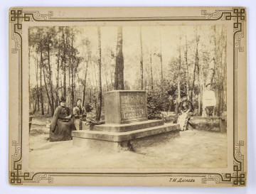 Fotografia pomnika upamiętniającego powstanie Ogrodu Saskiego w Lublinie. Na pierwszym planie widoczny pośrodku kamienny blok w kształcie prostopadłościanu ustawiony na podwyższeniu, do którego prowadzą dwa stopnie. Ujęcie pod kątem. Na jednej ze ścian pomnika wyryty w czterech rzędach napis: „1837 | EPOKA ZAŁOŻENIA | OGRODU DLA MIASTA | LUBLINA”. W głębi na drewnianych ławkach bez oparć siedzą: po lewej stronie dwie kobiety (starsza i młodsza) ubrane w stroje z epoki, po prawej kobieta w kraciastej sukni i w okularach (?). Za nią stoi mężczyzna w jasnej koszuli wypuszczonej na spodnie, spiętej w pasie. Na stopniach pomnika leżą złożone parasole. W tle wysokie drzewa parku. 
Fotografia sepiowana, naklejona na tekturę, otoczona ozdobną ramką w kolorze złotym o motywach geometryczno-roślinnych. W dolnej części, po prawej stronie nazwisko autora fotografii w języku rosyjskim.
